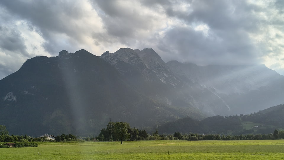 Podvečerní sluneční paprsky prorážející oblaka nad alpskými vrcholy